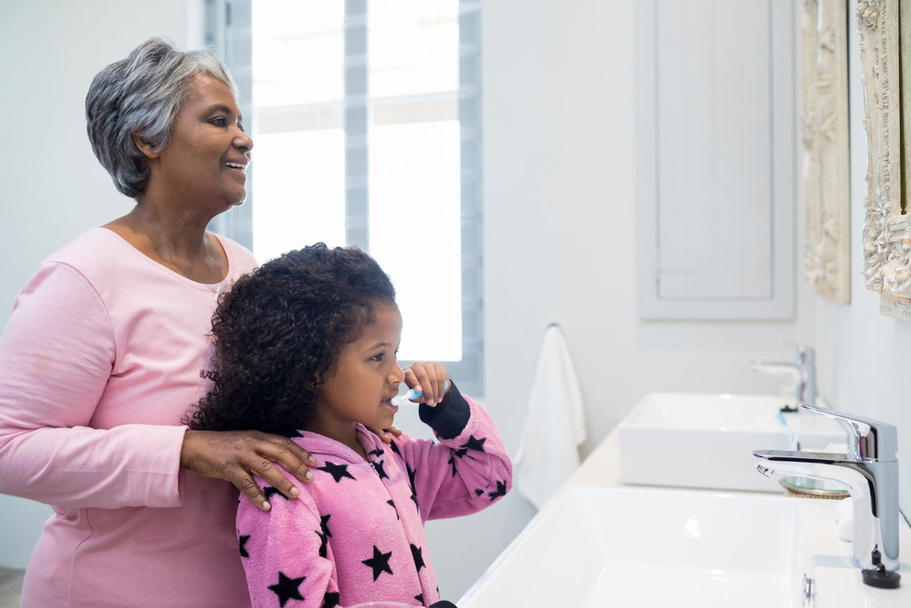 Little girl brushing her teeth with grandma watching